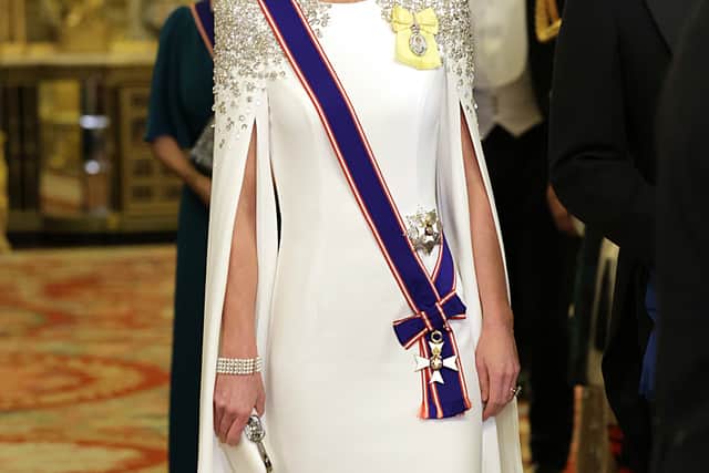She is shown composed, standing and facing forwards in a regal, caped white Jenny Packham floor-length evening dress with sparkling detail on the shoulders, and her go-to tiara, the Lover’s Knot.