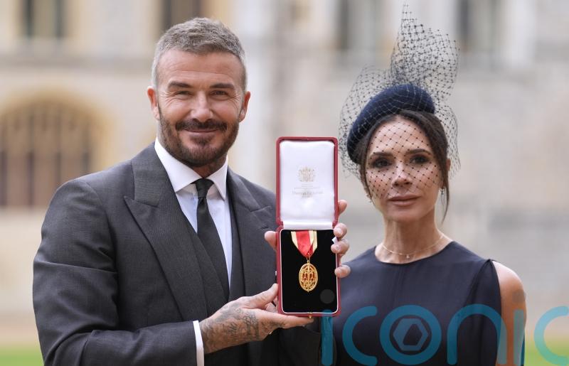 Sir David Beckham smiles next to Lady Victoria Beckham after being knighted